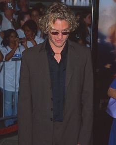 a man with curly hair and sunglasses standing in front of a crowd at an event