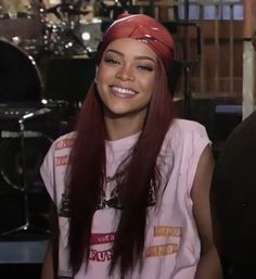 a woman with long red hair sitting in front of a drum set and smiling at the camera