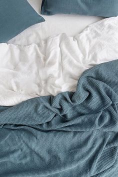 an unmade bed with white sheets and blue pillows