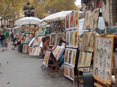 an outdoor art market with people looking at paintings and umbrellas on the side walk