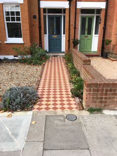 a brick house with a green door and checkerboard pattern on the sidewalk next to it