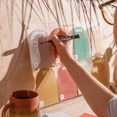 a person writing on a piece of paper next to a coffee mug and eyeglasses