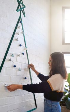 a woman is decorating a christmas tree on the wall with green tape and beads