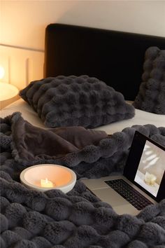 a laptop computer sitting on top of a bed next to pillows and a lit candle