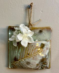 a white flower sitting on top of a green square tile wall hanging ornament