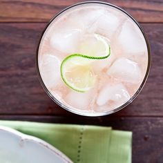 a close up of a drink in a glass with ice and lime slices on the rim