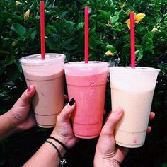 three people holding up drinks in front of some bushes and flowers with red straws