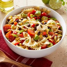 a white bowl filled with pasta salad next to a wooden spoon and glass of olive oil