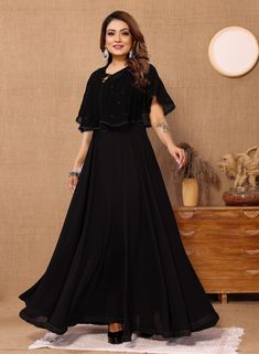 This elegant black long gown with cape is the perfect choice for a formal event or special occasion. Made from Georgette fabric with a Butter Crepe inner lining, this dress features a stylish Koti design and intricate lace work detailing, adding a touch of sophistication to your ensemble. The classic black color ensures versatility and timeless style, making it a must-have addition to your wardrobe. PRODUCT DETAILS :- Black solid maxi dress Round neck Short, flared sleeves Embellished detail Max Georgette Maxi Dress With Cape Sleeves, Fitted Georgette Gown With Cape Sleeves, Festive Gala Gown With Cape Sleeves, Fitted Cape Maxi Dress For Wedding, Festive Gown With Cape Sleeves For Gala, Wedding Cape Maxi Dress Fitted, Georgette Gown With Cape Sleeves, Fitted Cape Maxi Dress For Gala, Georgette Maxi Dress With Cape Sleeves For Party