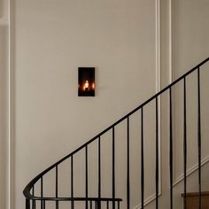 two candles are lit on the wall next to a stair case in a white room