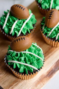 three cupcakes with green frosting and football decorations on top, sitting on a cutting board