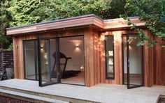 a small wooden building with glass doors on the front and side windows, sitting next to trees