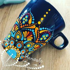 a blue coffee mug with colorful designs on it sitting on top of a wooden table