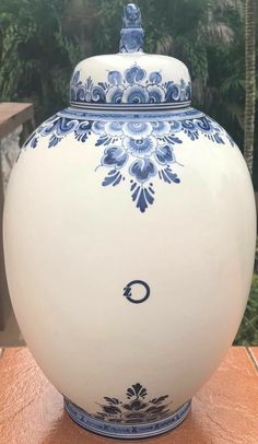 a blue and white vase sitting on top of a wooden table next to some trees