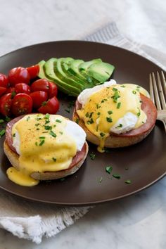 two eggs benedicts with tomatoes and cucumbers on a plate next to a fork