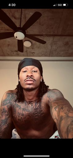 a man with tattoos on his chest wearing a bandana and looking at the camera