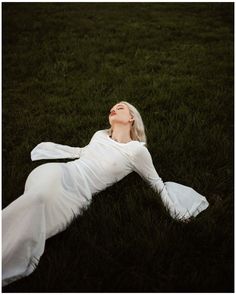 a woman laying in the grass with her eyes closed wearing a white dress and head scarf