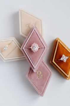 three different colored jewelry boxes with diamond rings in them on a white surface, one containing an engagement ring and the other containing two diamonds