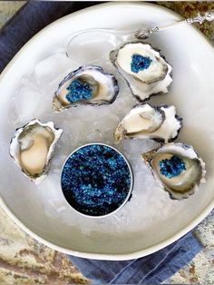 several oysters on ice in a white bowl with blue glitter and a silver spoon