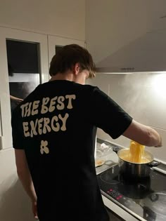 the man is cooking in the kitchen with his hand on the burner and stirring something