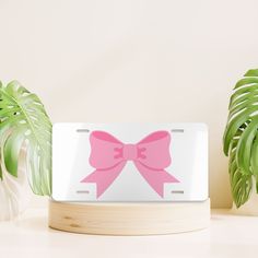 a pink bow on a white license plate next to some green plants and a potted plant