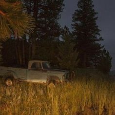 an old pick up truck is parked in the middle of a grassy field at night