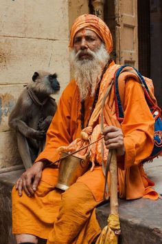 an old man sitting next to a monkey and holding a metal cup in his hand