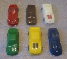 six toy cars are lined up in a row on the floor, all different colors