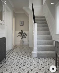 a white and gray hallway with stairs, potted plant and pictures on the wall