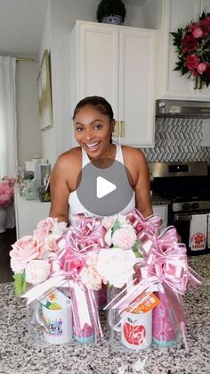 a woman standing in front of a kitchen counter with pink flowers and cans on it