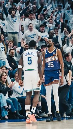 two basketball players are talking to each other in front of an arena full of people