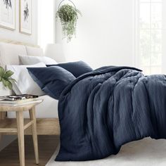 a bed with blue sheets and pillows in a white room next to a wooden table