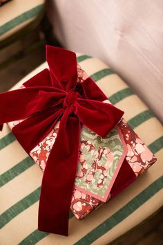 a present wrapped in red ribbon sitting on top of a green and white striped chair