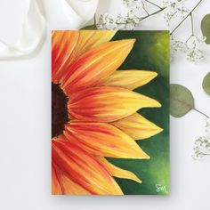 a painting of a sunflower on a card next to some white flowers and leaves