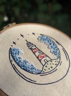 a close up of a cross stitch on a piece of cloth with a lighthouse in the middle