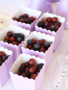 grapes and raspberries are in small purple boxes on a table with water glasses