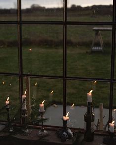 candles are lit in front of a window with the view of a grassy field outside