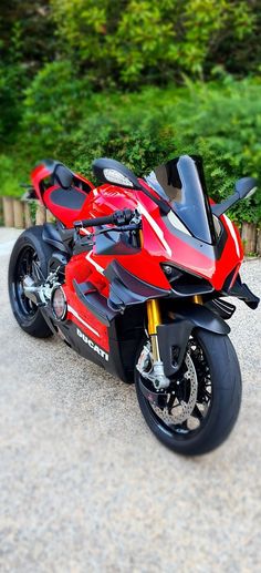 a red and black motorcycle parked on top of a gravel road next to some trees