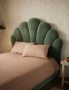 a bed with a green headboard and two pillows on it in a room that has white walls