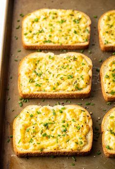 six pieces of bread with cheese and chives on them sitting on a baking sheet