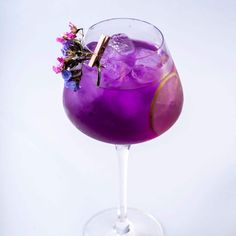 a purple drink in a wine glass with flowers on the rim