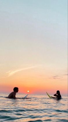 two people in the water with surfboards at sunset