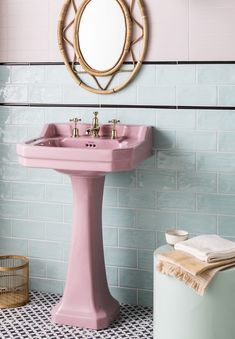 a pink pedestal sink in a bathroom next to a round mirror and blue tiled walls