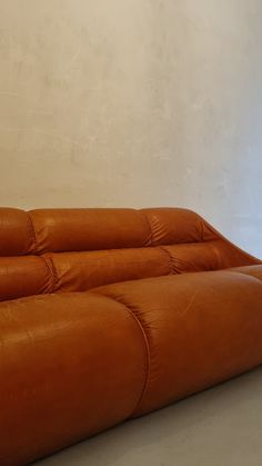 an orange leather couch sitting on top of a white floor next to a wall and window