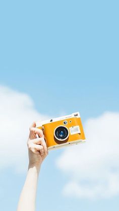 a person holding an orange camera up in the air with a blue sky behind them