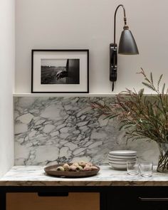 a marble counter top with plates and bowls on it next to a wall mounted light