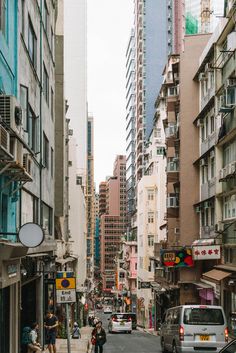 people are walking on the sidewalk in an urban area with tall buildings and parked cars