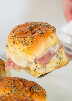 a ham and cheese slider being held by a person's hand over a white plate