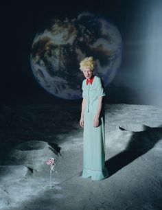 a woman standing on the moon with her hands in her pockets and wearing a blue dress