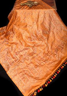 With design influences from the Mughals, the Royals of Kashmir and exquisite weaving techniques from China that were brought to India by Parsi merchants, comes the majestic Tanchoi Jamawar fabric! This pure Satin Silk Banarasi saree in a soft Marmalade shade of Orange  and features Tanchoi Jamawar paisley design in Green, Orange, and Red shades. Expertly woven with smooth and lustrous fabric, the saree showcases fine paisley patterns in complementary hues, with no cut or floating threads on the reverse side. SILK MARK CERTIFIED This saree is ready to wear with fall and pico done. Handmade silk tassels adorn the pallu and add more grace to it. An unstitched blouse fabric is included. *Note: There may be minor variations in the shade, the texture of the product. Hues/textures show differentl Jamawaar Fabric, Elegant Ceremonial Dupatta With Woven Motifs, Gold Silk Dupatta With Woven Motifs, Elegant Katan Silk Saree With Woven Motifs, Bohemian Silk Dupatta For Ceremonial Use, Ceremonial Bohemian Silk Dupatta, Ceremonial Silk Dupatta With Woven Motifs, Elegant Jamawar Dupatta With Woven Motifs, Traditional Pashmina Silk Scarf With Patterns